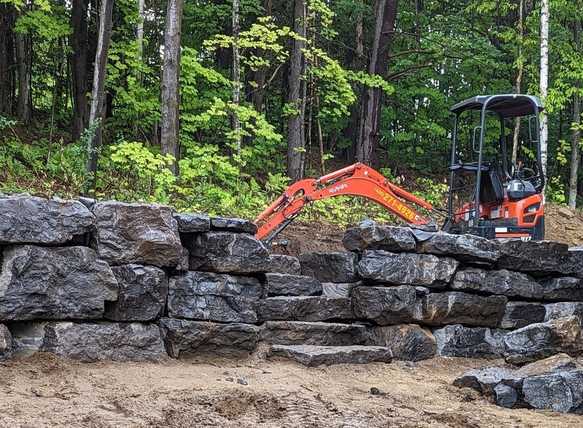 Une excavatrice travaille sur un mur de pierre dans les bois.