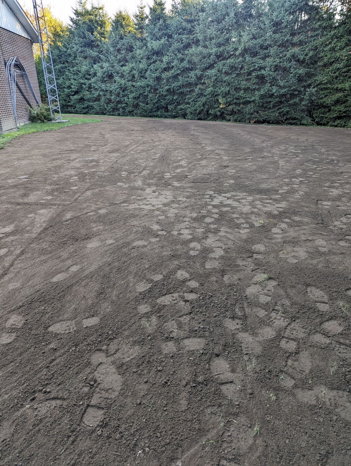 Un grand champ de terre avec des arbres en arrière-plan et une maison en arrière-plan.