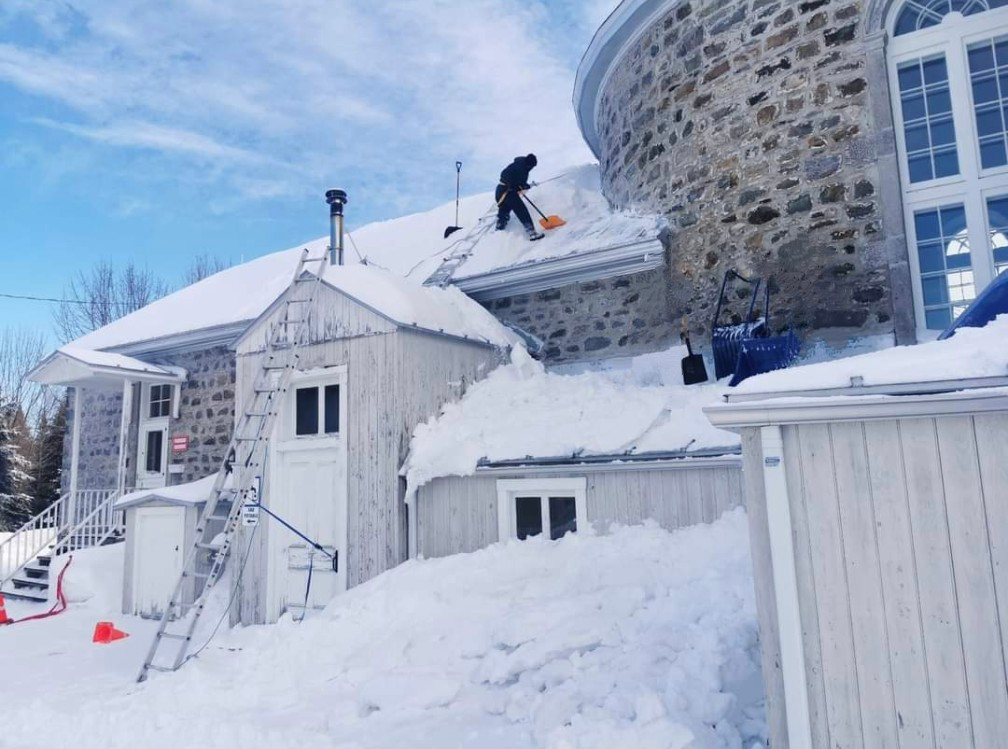 Un homme pellete la neige du toit d'une maison.