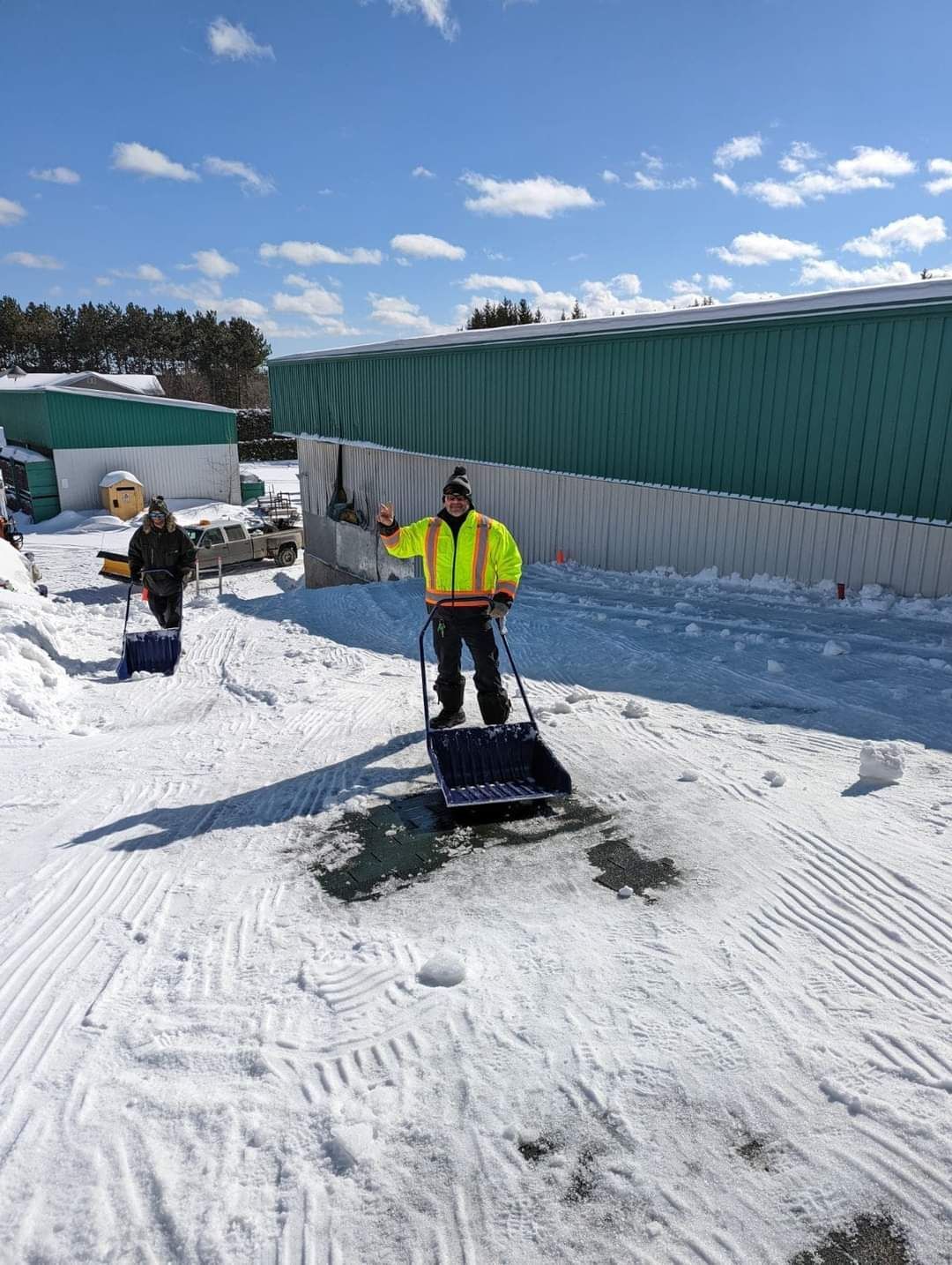 Un homme pellete de la neige devant un immeuble.