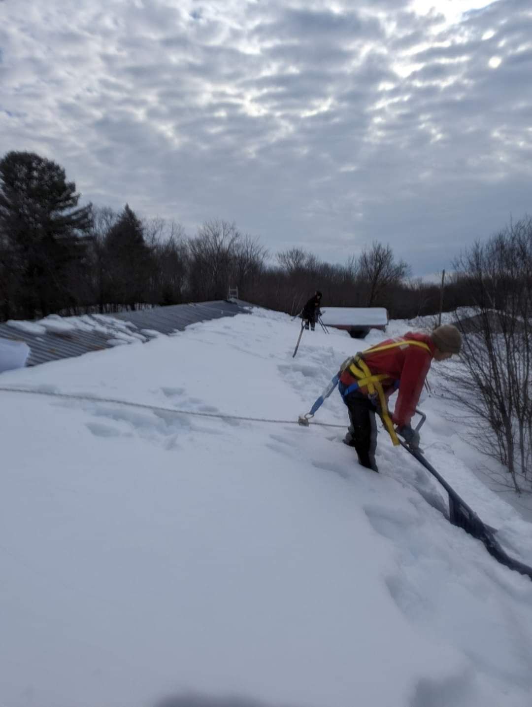 Un homme pellete la neige du toit d'une maison