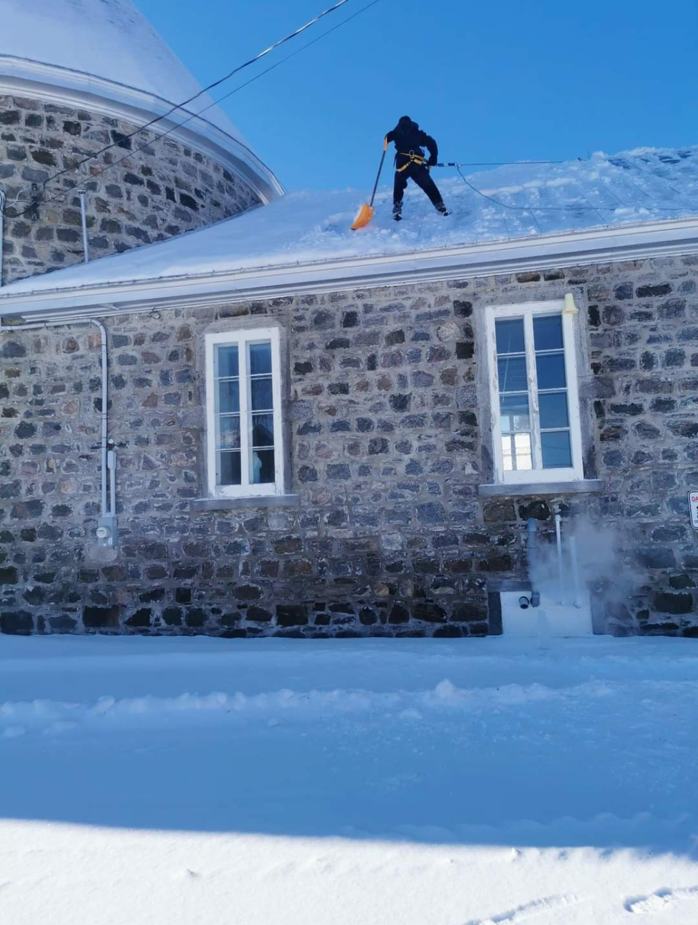 Un homme pellete la neige du toit d'un bâtiment en pierre