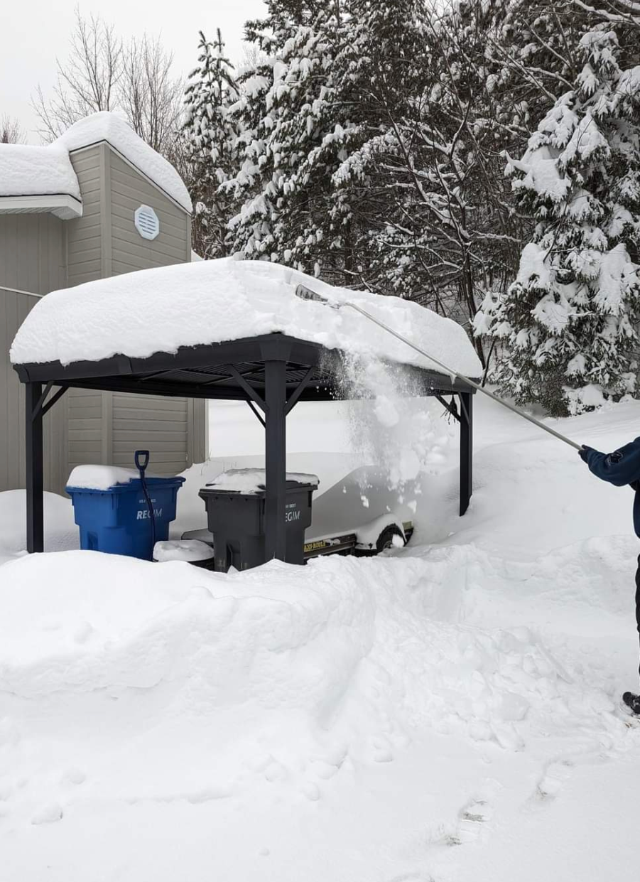 Une personne pellete de la neige devant un immeuble.