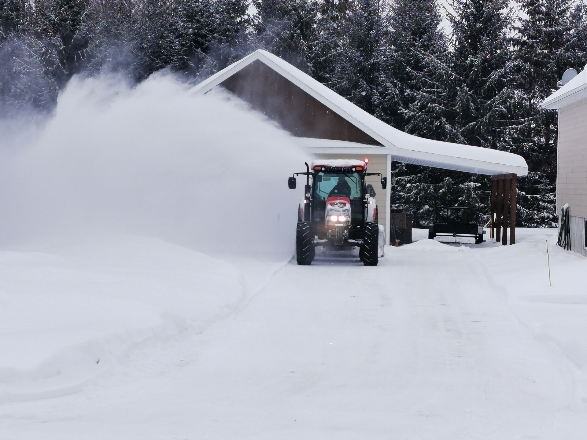 Un tracteur déblaye la neige d'une allée devant une maison.
