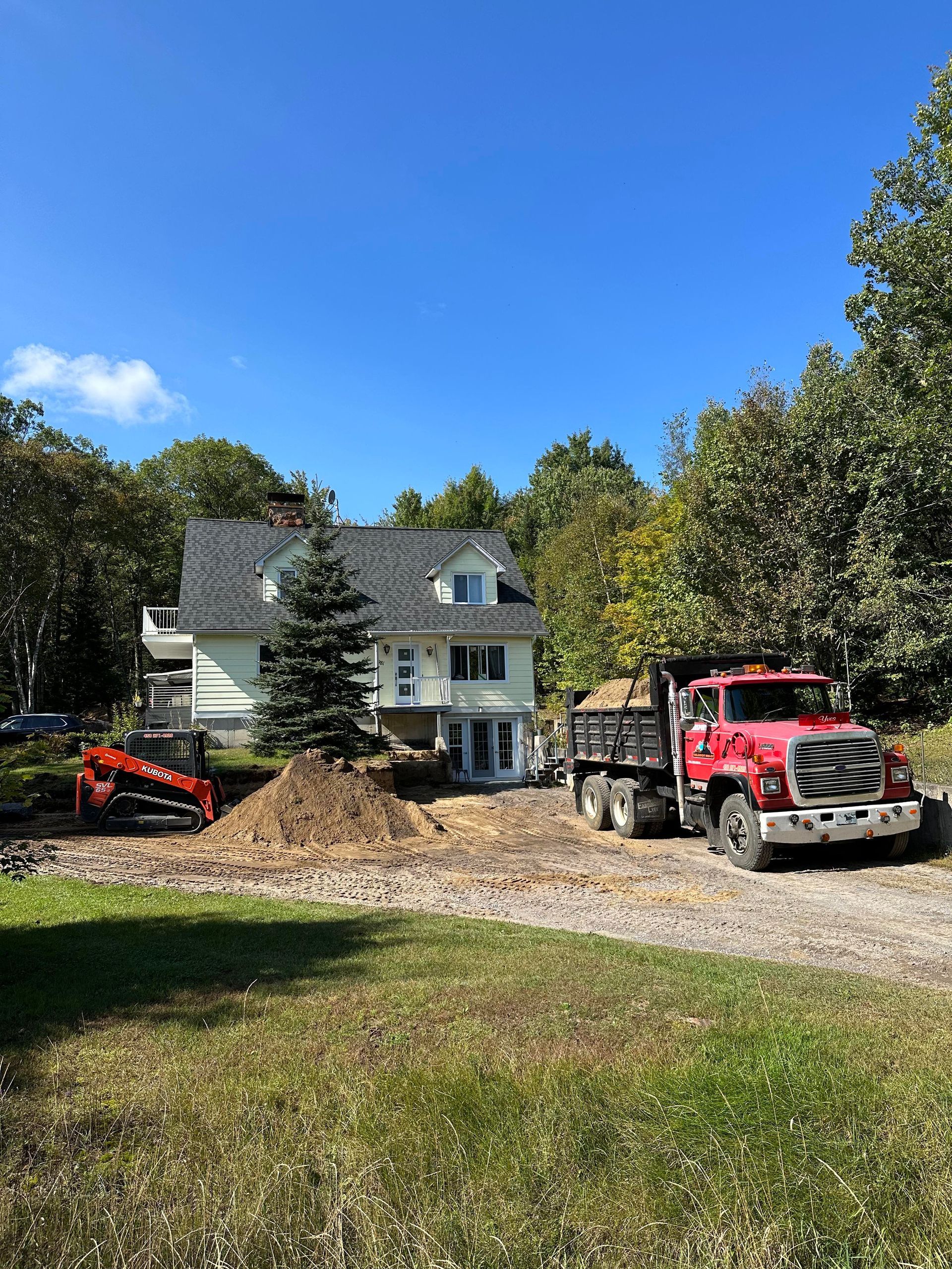 Un camion à benne rouge est garé devant une maison.