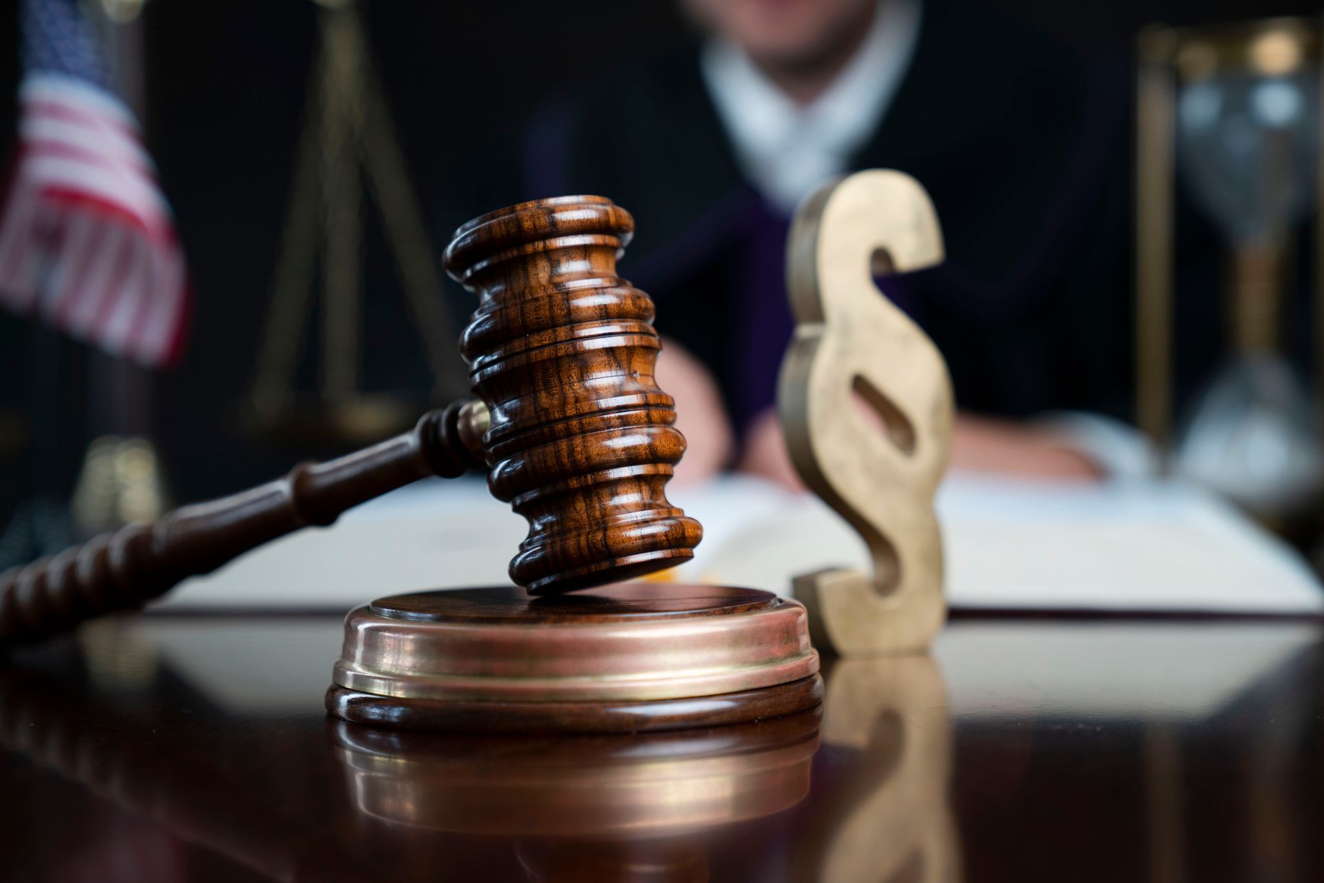 Wooden gavel on a table with a judge in the background and legal symbols.