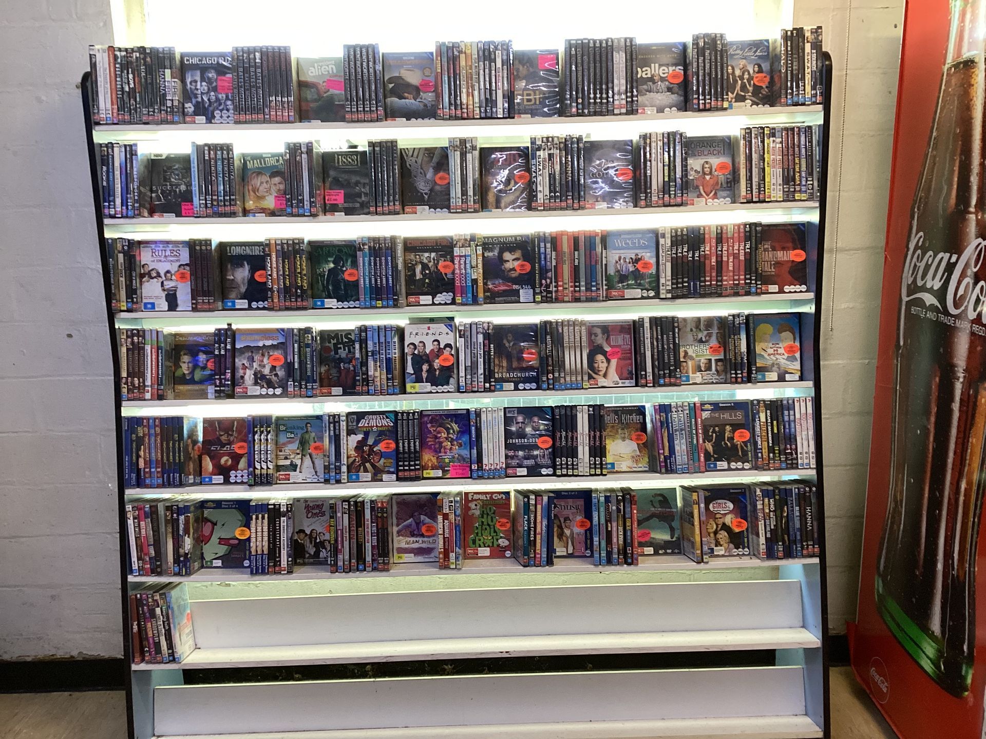 A Shelf Full of Dvds Next to a Coca Cola Machine — West End Cash Store In Proserpine, QLD