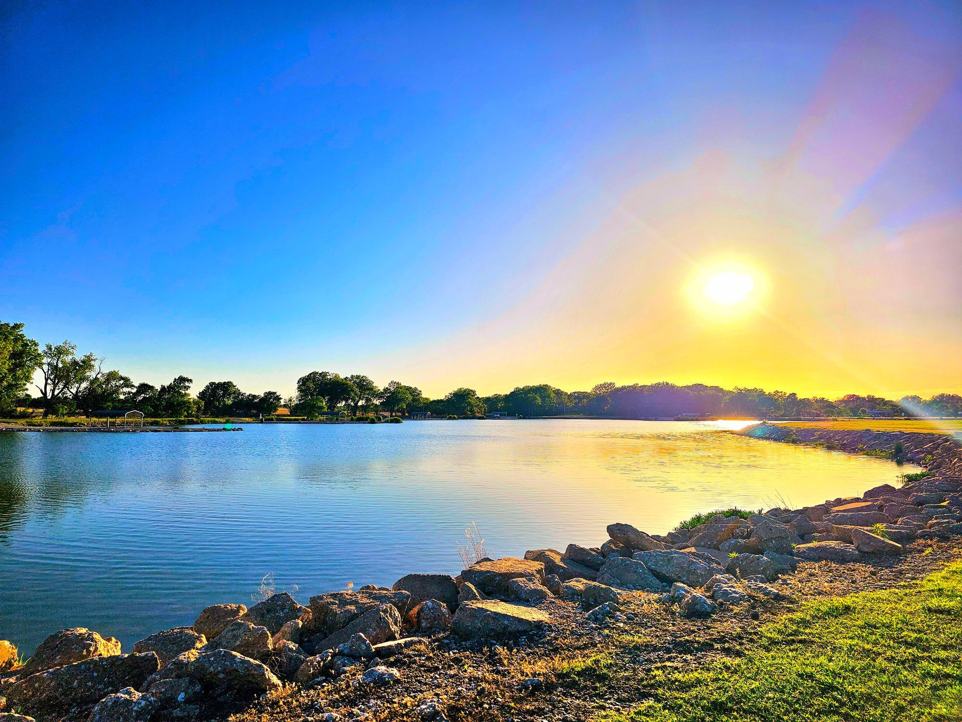The sun is setting over a lake with trees in the background.