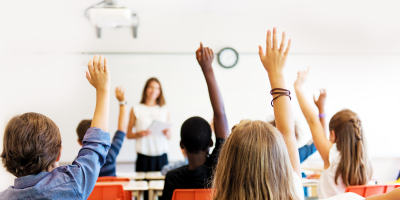 A group of children are raising their hands in a classroom to answer a question.