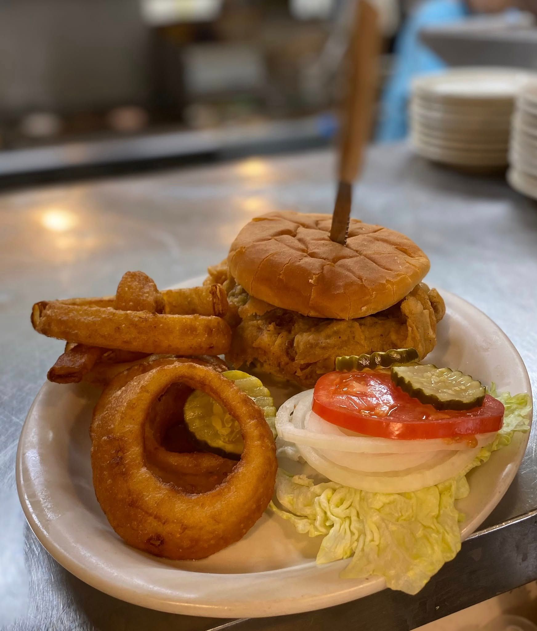 A white plate topped with a hamburger , onion rings , lettuce and tomatoes.
