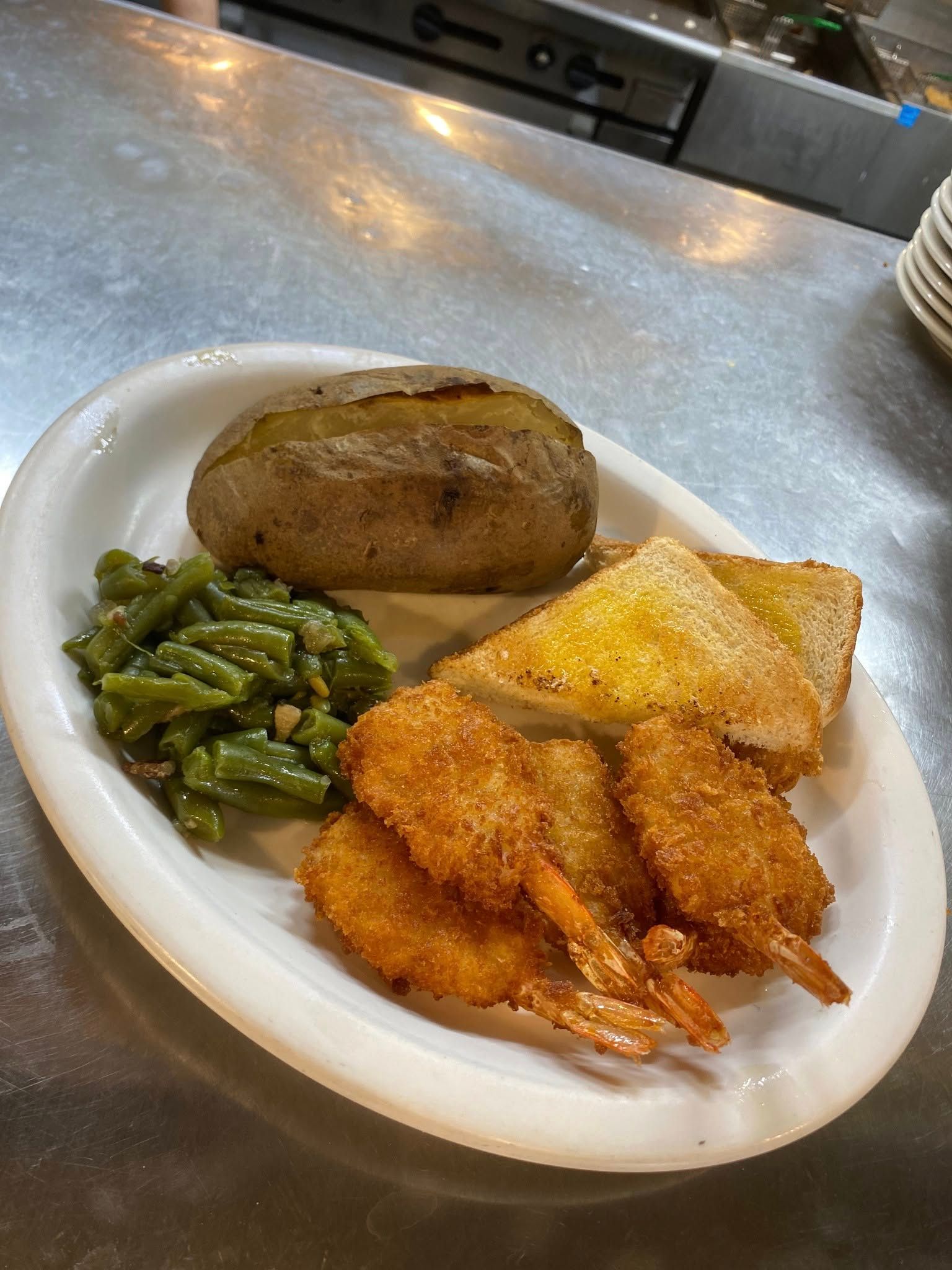 A plate of food with shrimp , green beans , toast and a baked potato on a table.