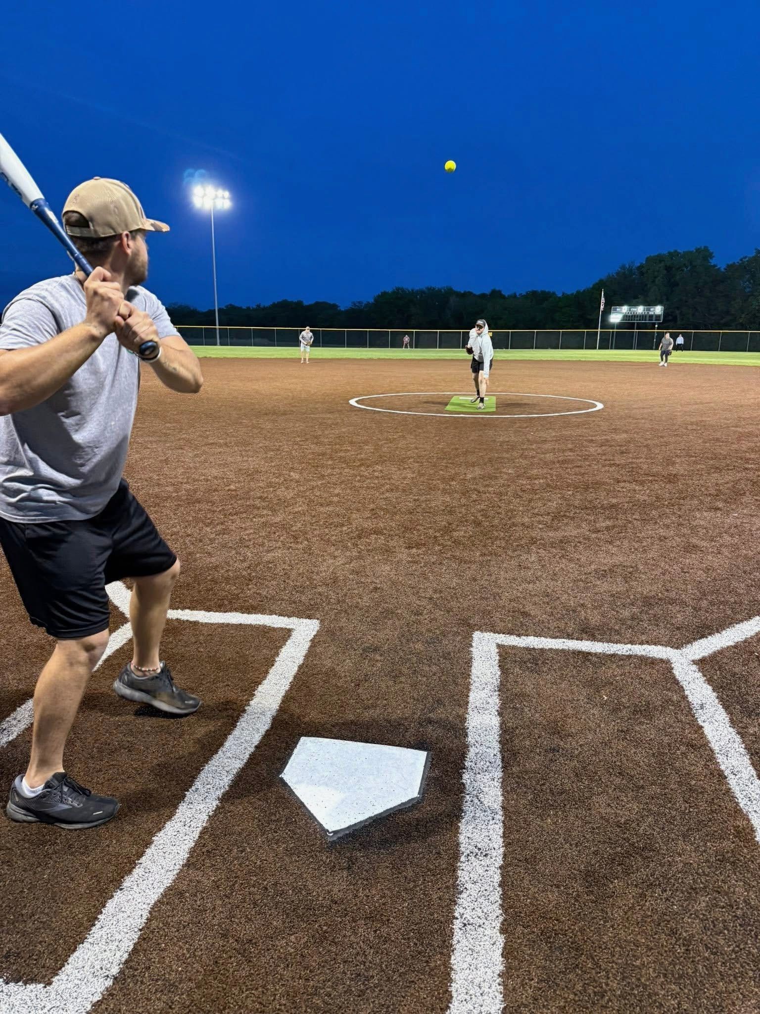 A man is swinging a bat at a baseball on a field at night.