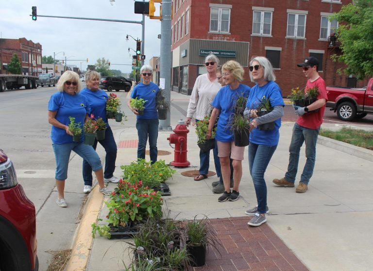 A group of people standing on a sidewalk holding potted plants.