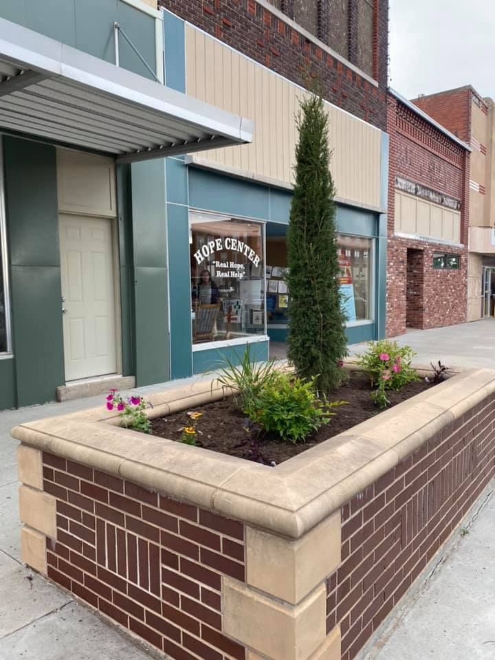 A brick planter with flowers and trees in front of a building.