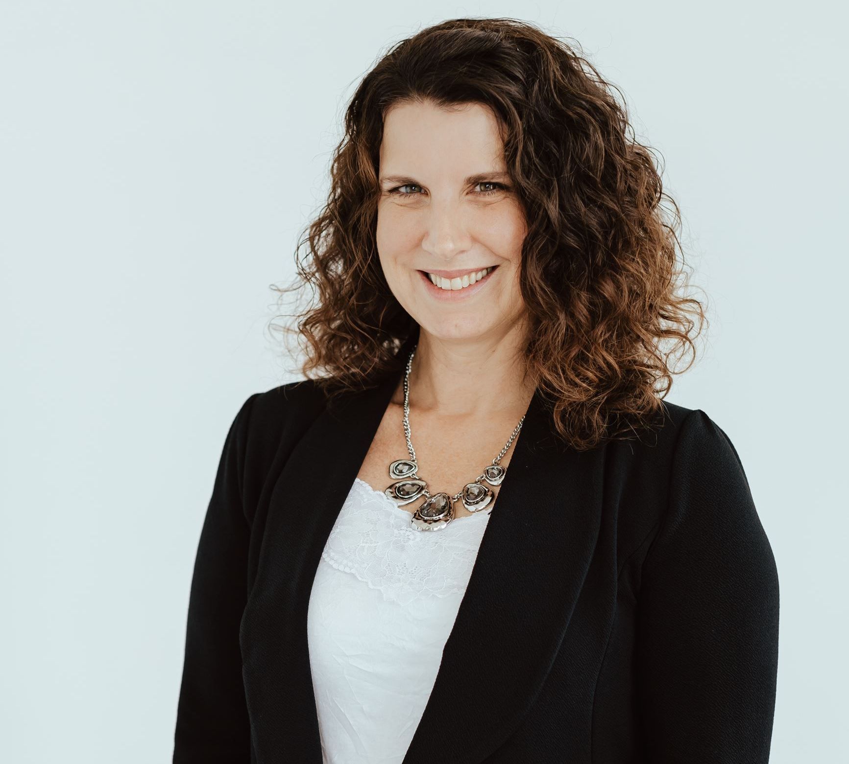 A woman wearing a black jacket and a necklace is smiling for the camera.