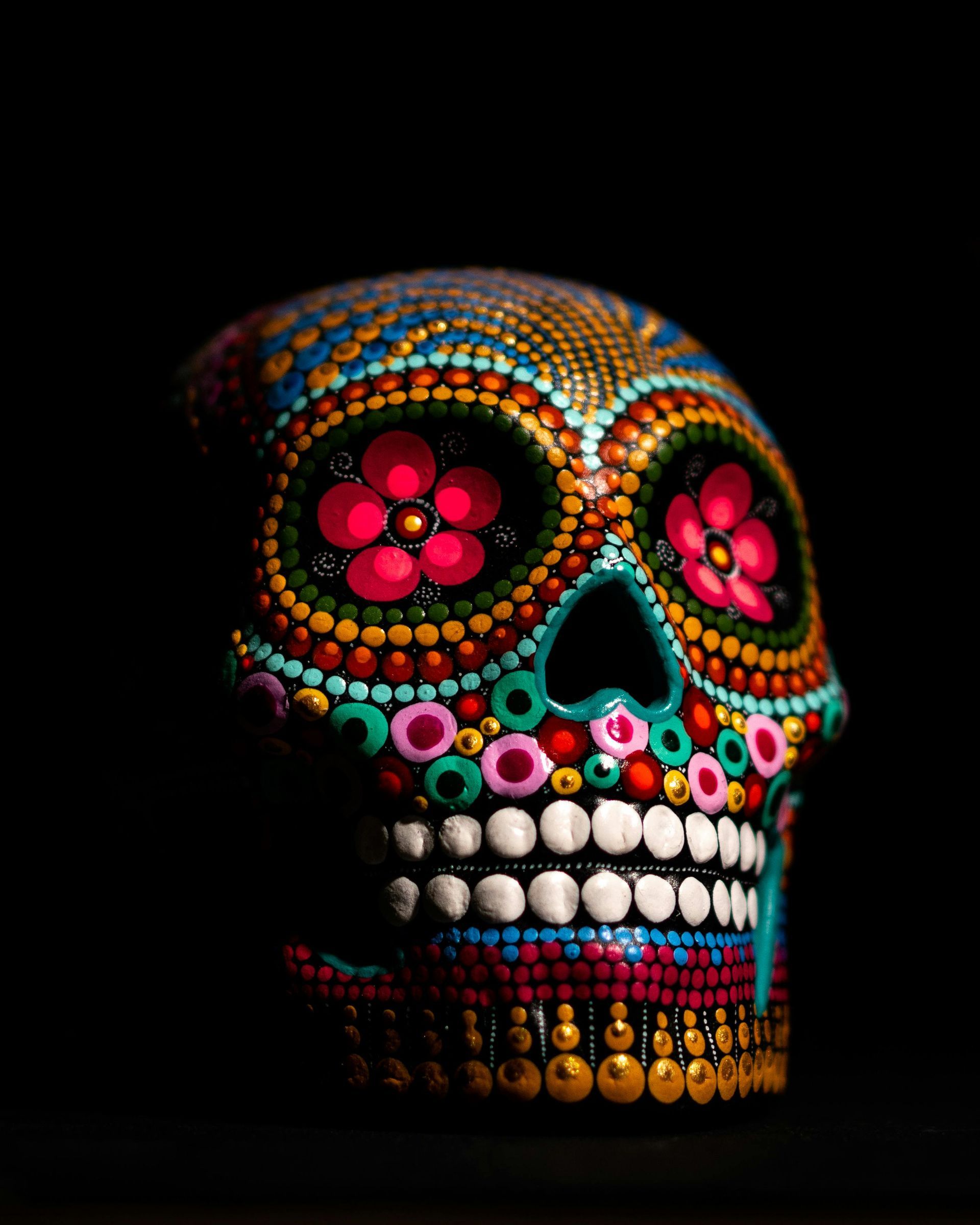 Colorful Day of the Dead skull with dot and floral decorations against a black background.
