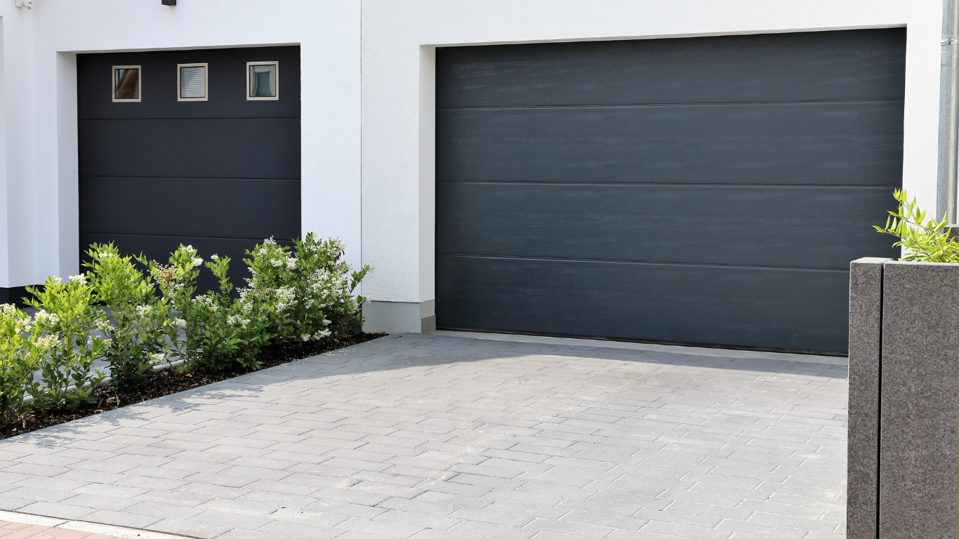 Gray garage doors on a white building, concrete driveway, and bushes.