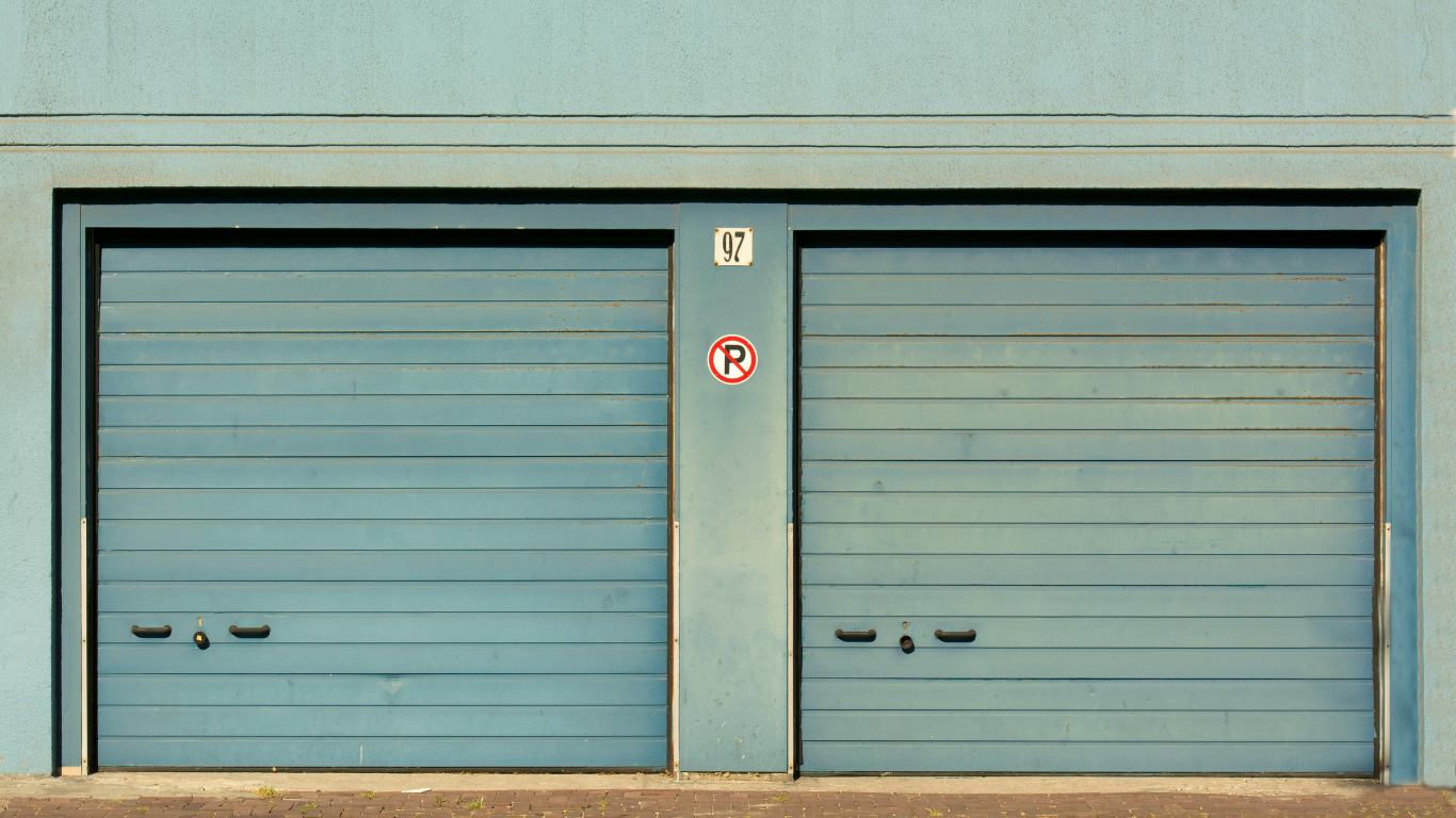 Two blue garage doors in a teal building with a small circular sign between them.