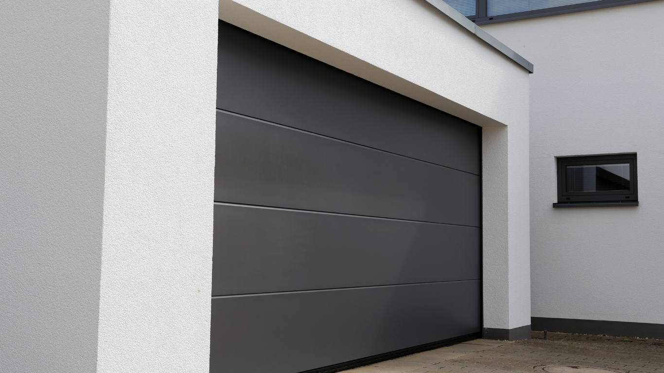 Gray garage door on a white building, small dark window visible.