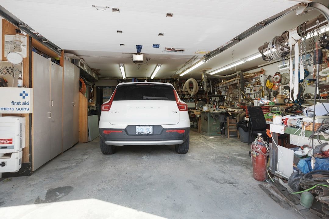 White SUV parked in a cluttered garage, with tools and equipment lining the walls.