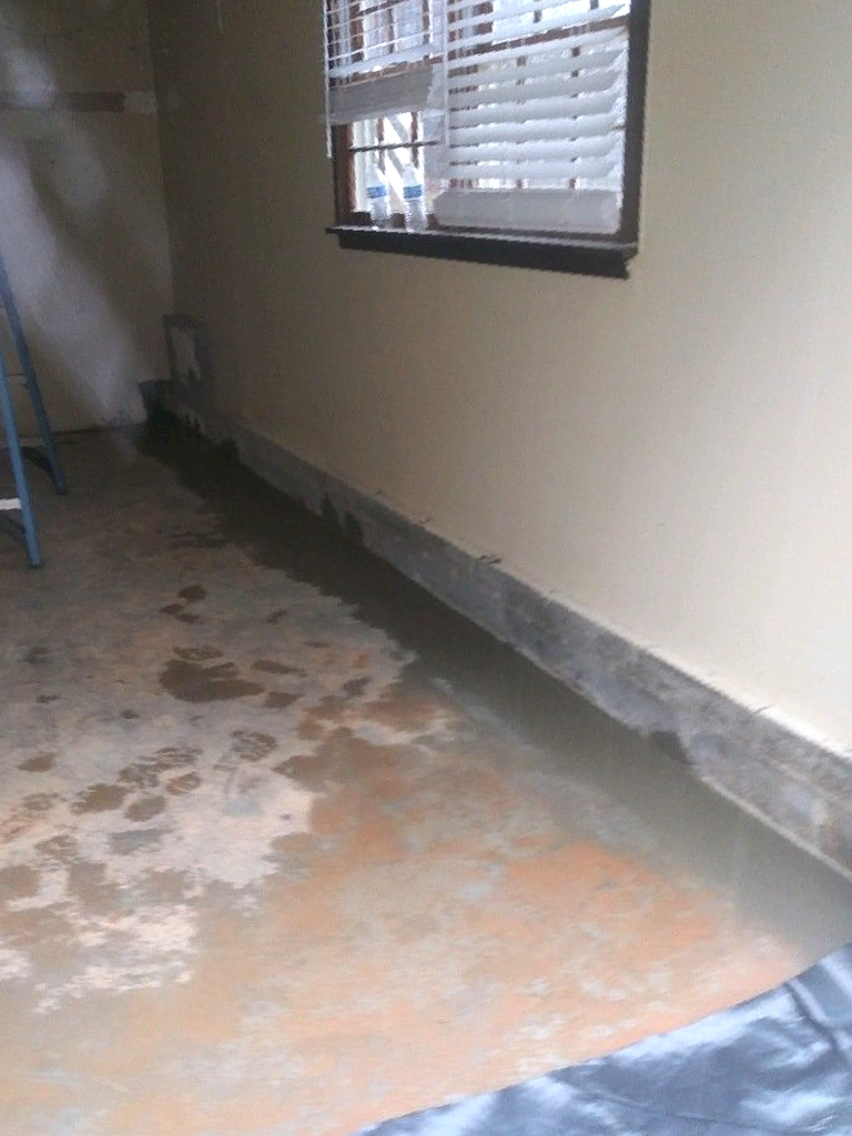 Flooded basement with standing water. Wall and window visible. Dark trim line near floor.