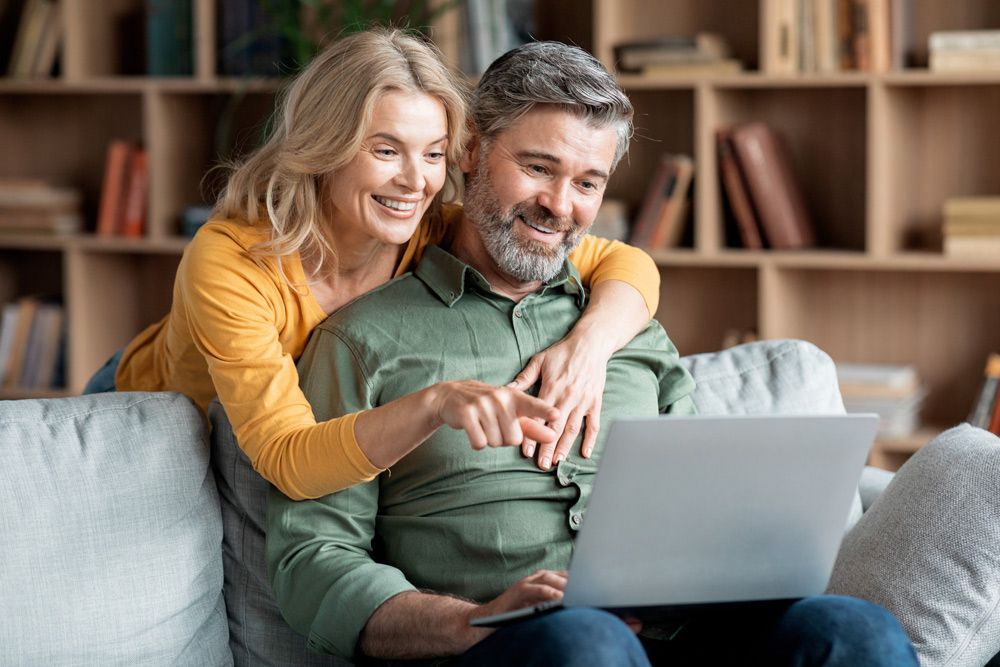 A Man and A Woman Are Sitting on A Couch Looking at A Laptop — Tech Bias in Redbank Plains, QLD