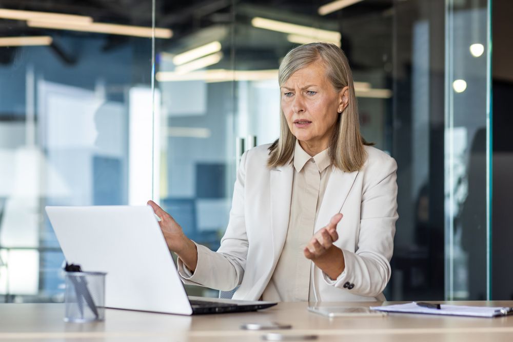 An Older Woman Is Sitting at A Desk in Front of A Laptop Computer — Tech Bias in Redbank Plains, QLD