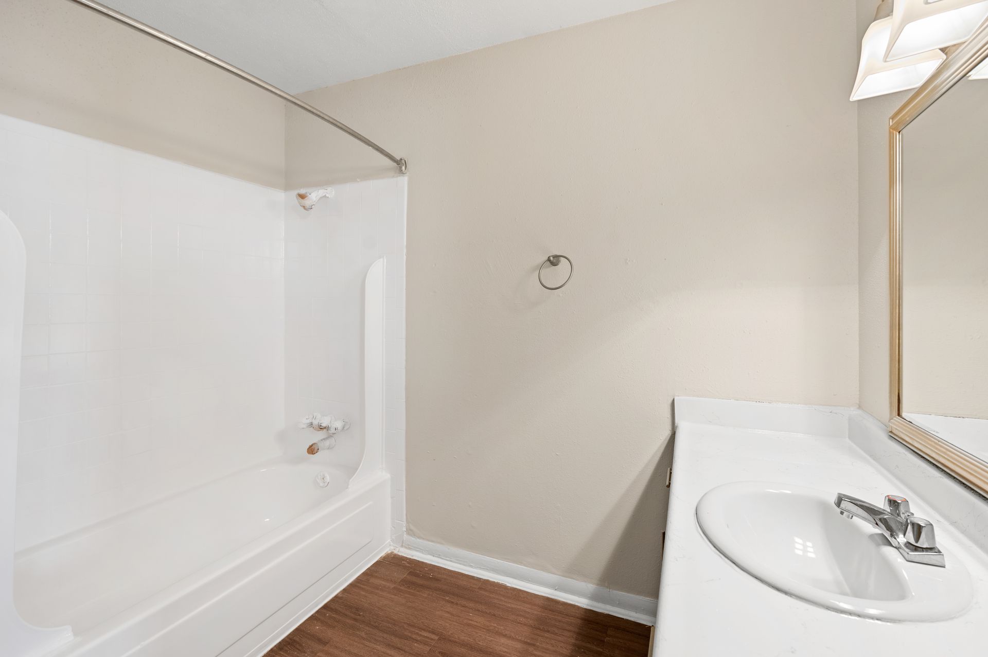 Bathroom with white tub, sink, and beige walls, brown floor.