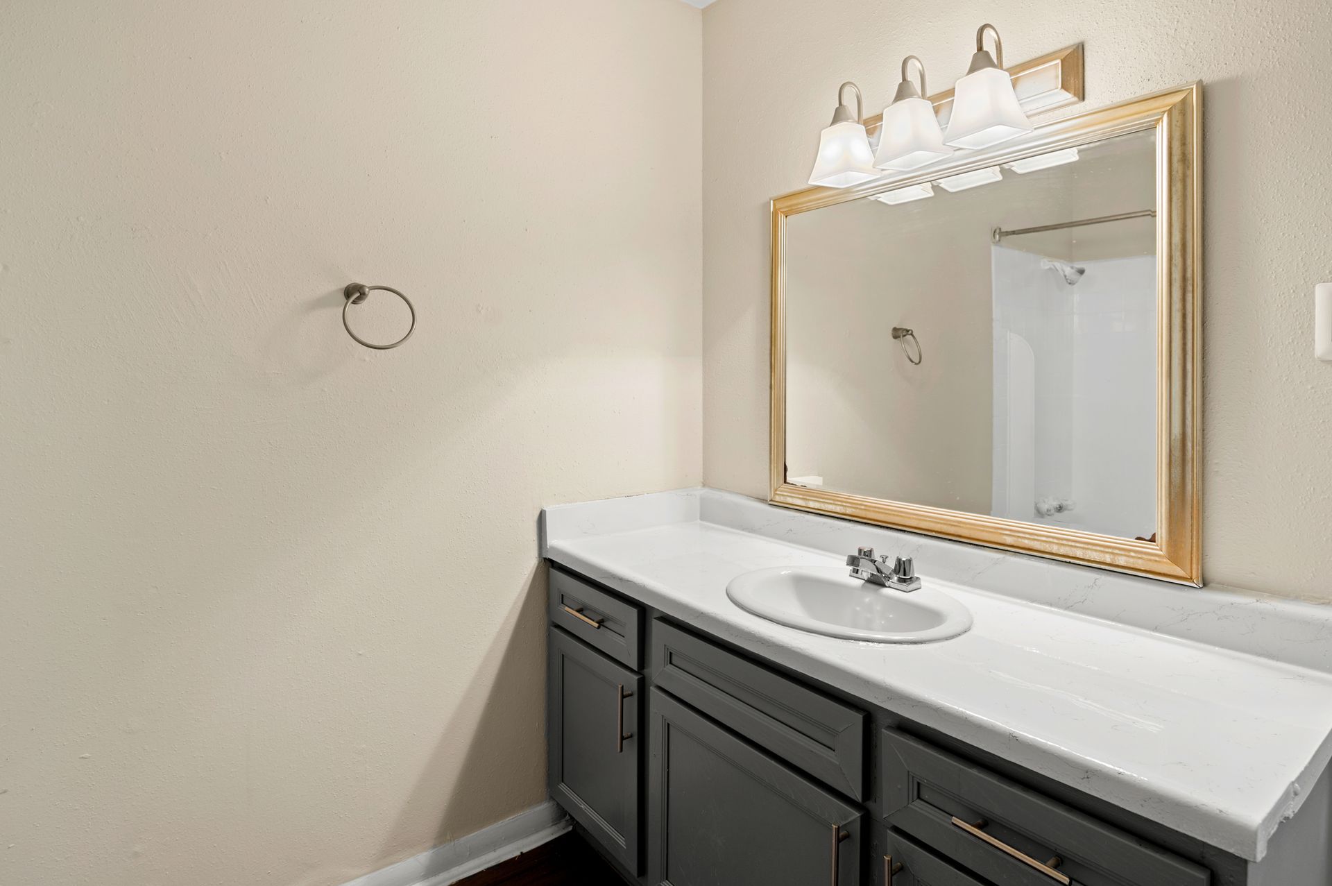 Bathroom with gray cabinets, white countertop, gold-framed mirror, and light fixture.