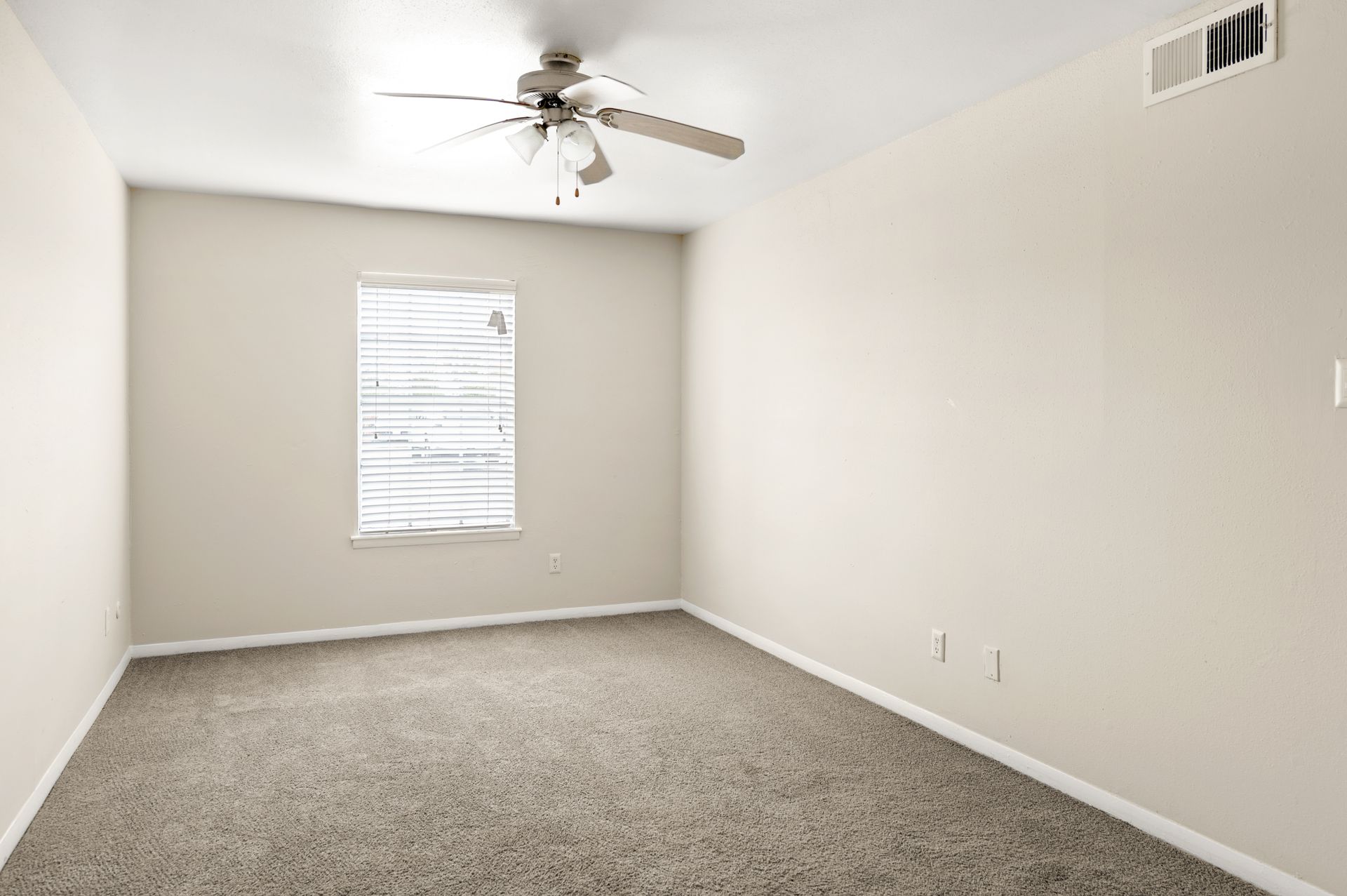 Empty room with beige walls, carpet, window with blinds, and ceiling fan.