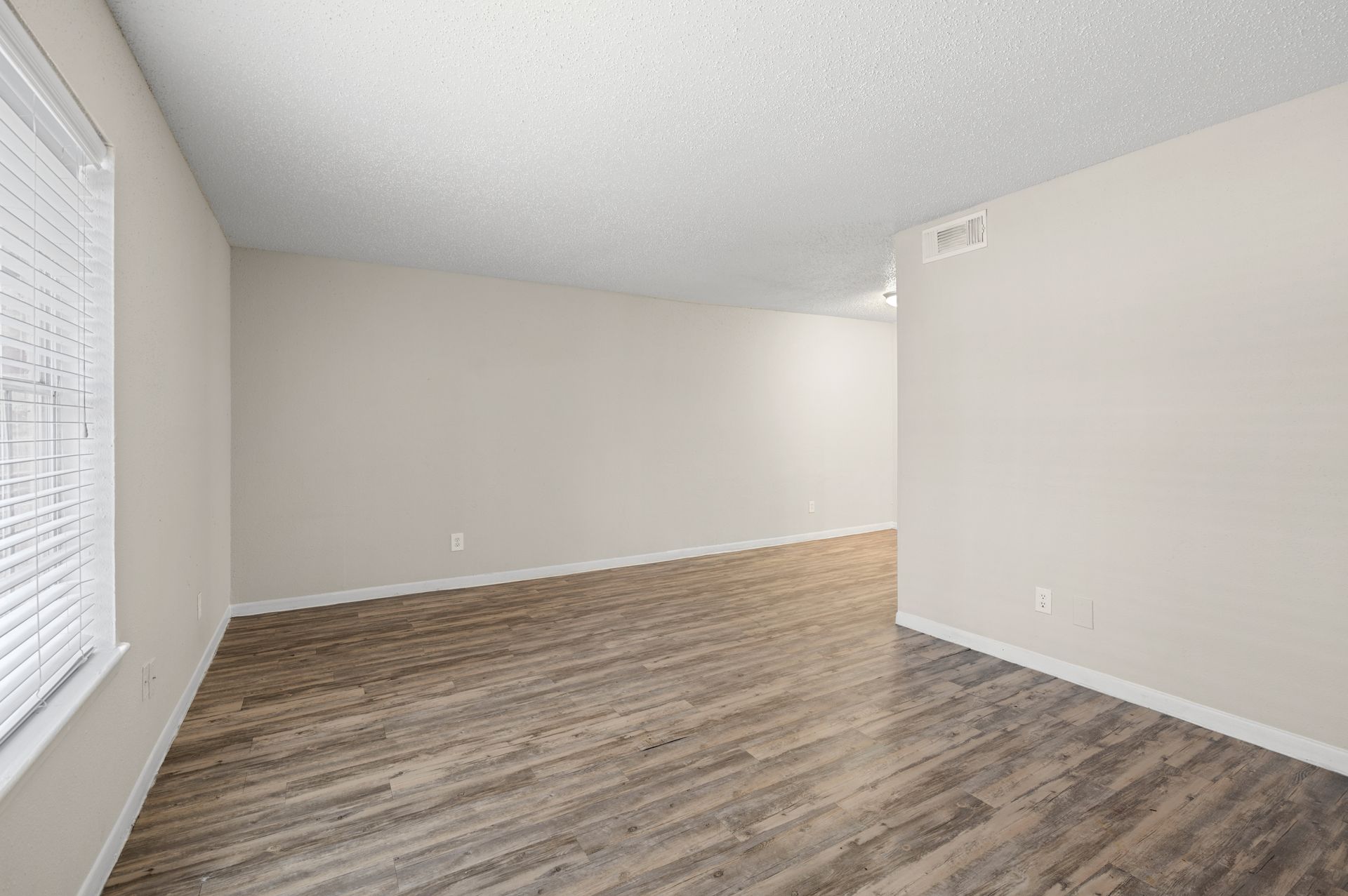 Empty room with beige walls, wooden floors, and a window with blinds.