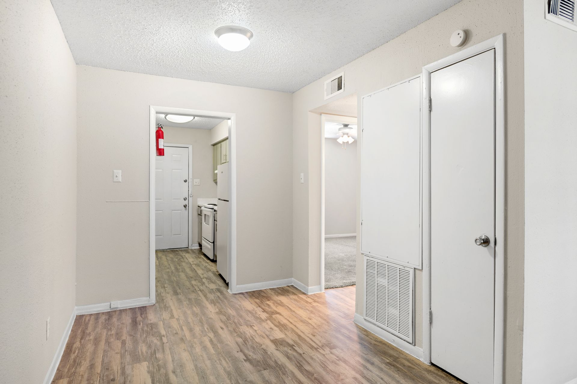 Interior apartment hallway with wooden floors, white doors, and a fire extinguisher.