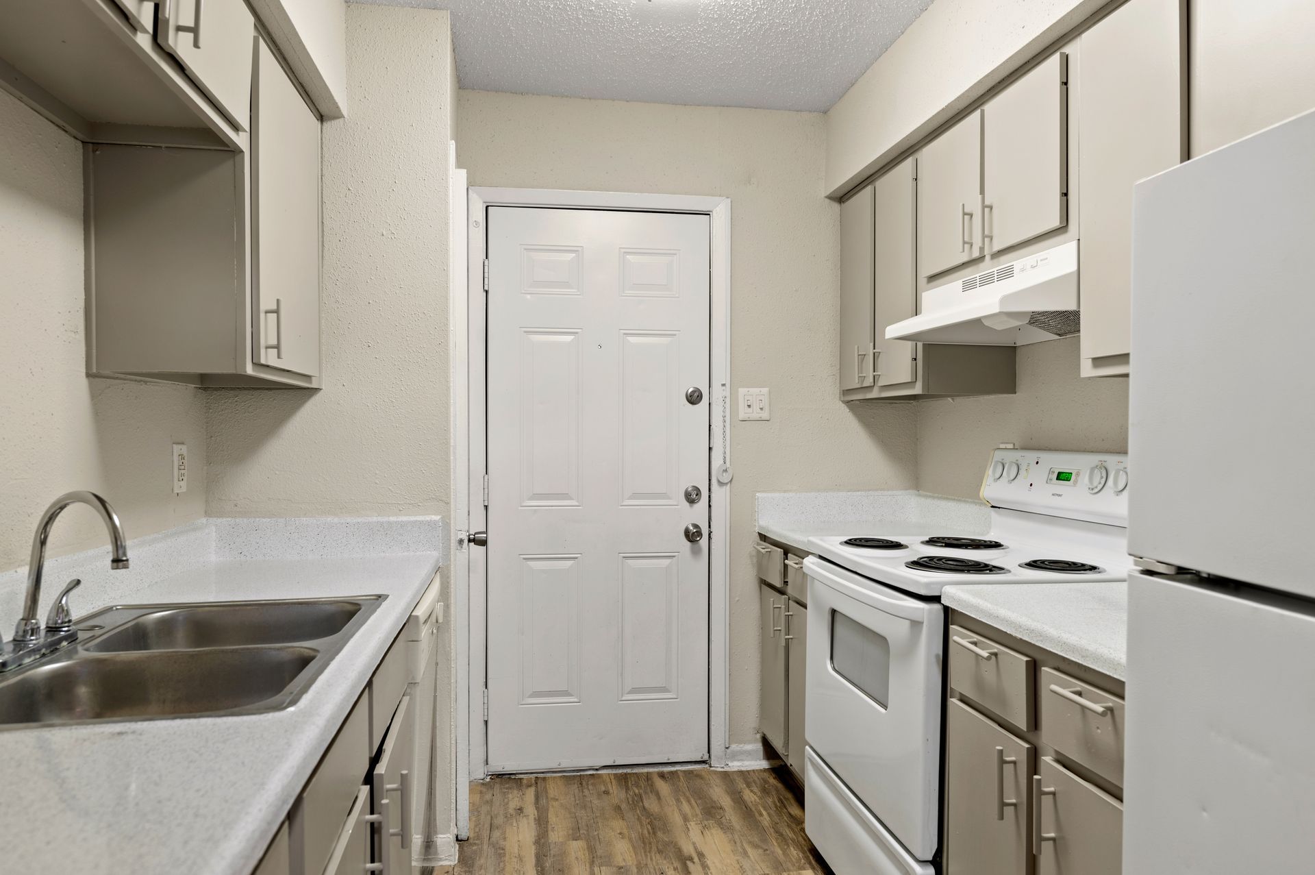 Kitchen with white appliances, light cabinets, and a door in the background.