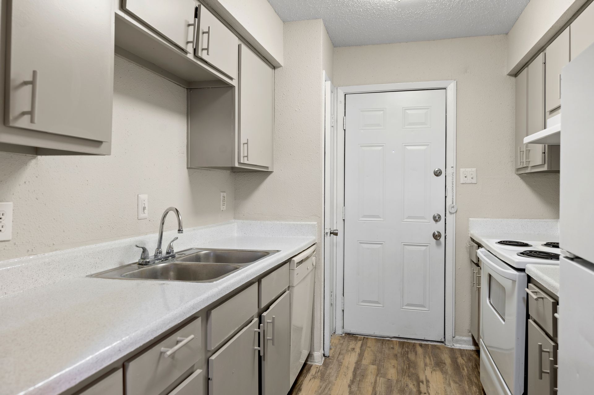 Kitchen with gray cabinets, white countertops, appliances, and a door.