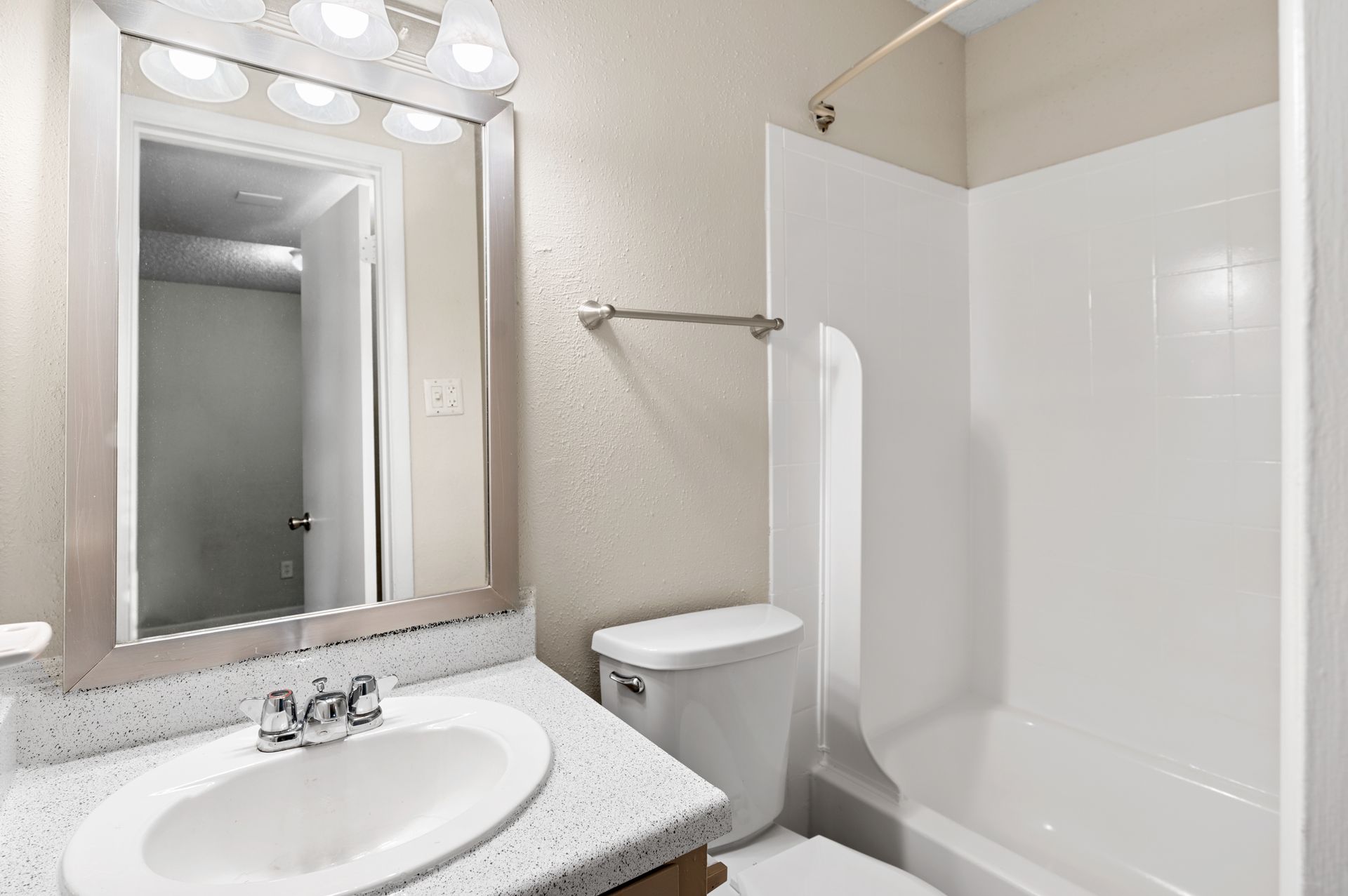 Bathroom with white fixtures, speckled countertop, large mirror, and open doorway.