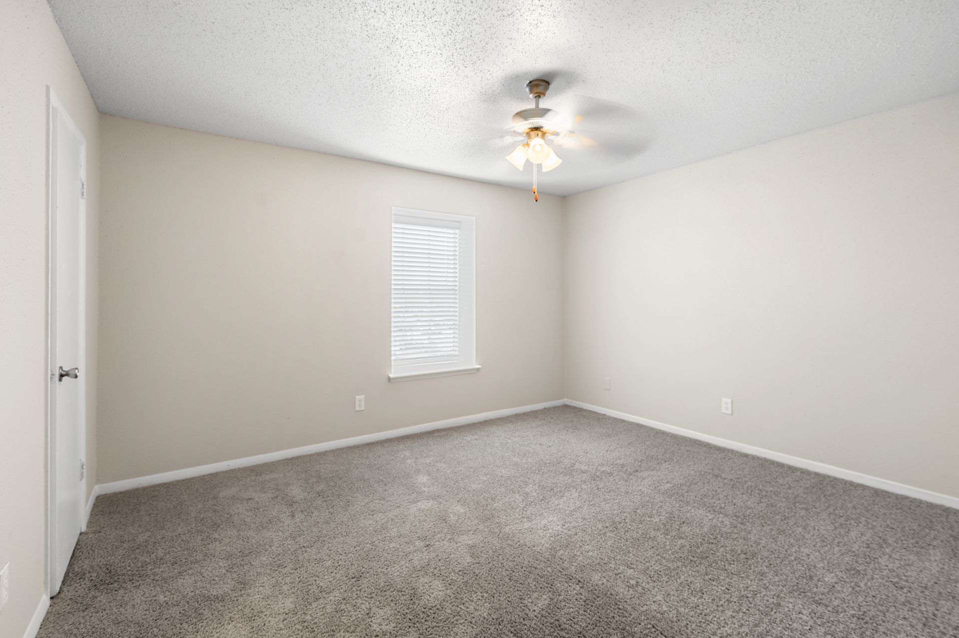Empty bedroom with gray carpet, beige walls, and a ceiling fan.