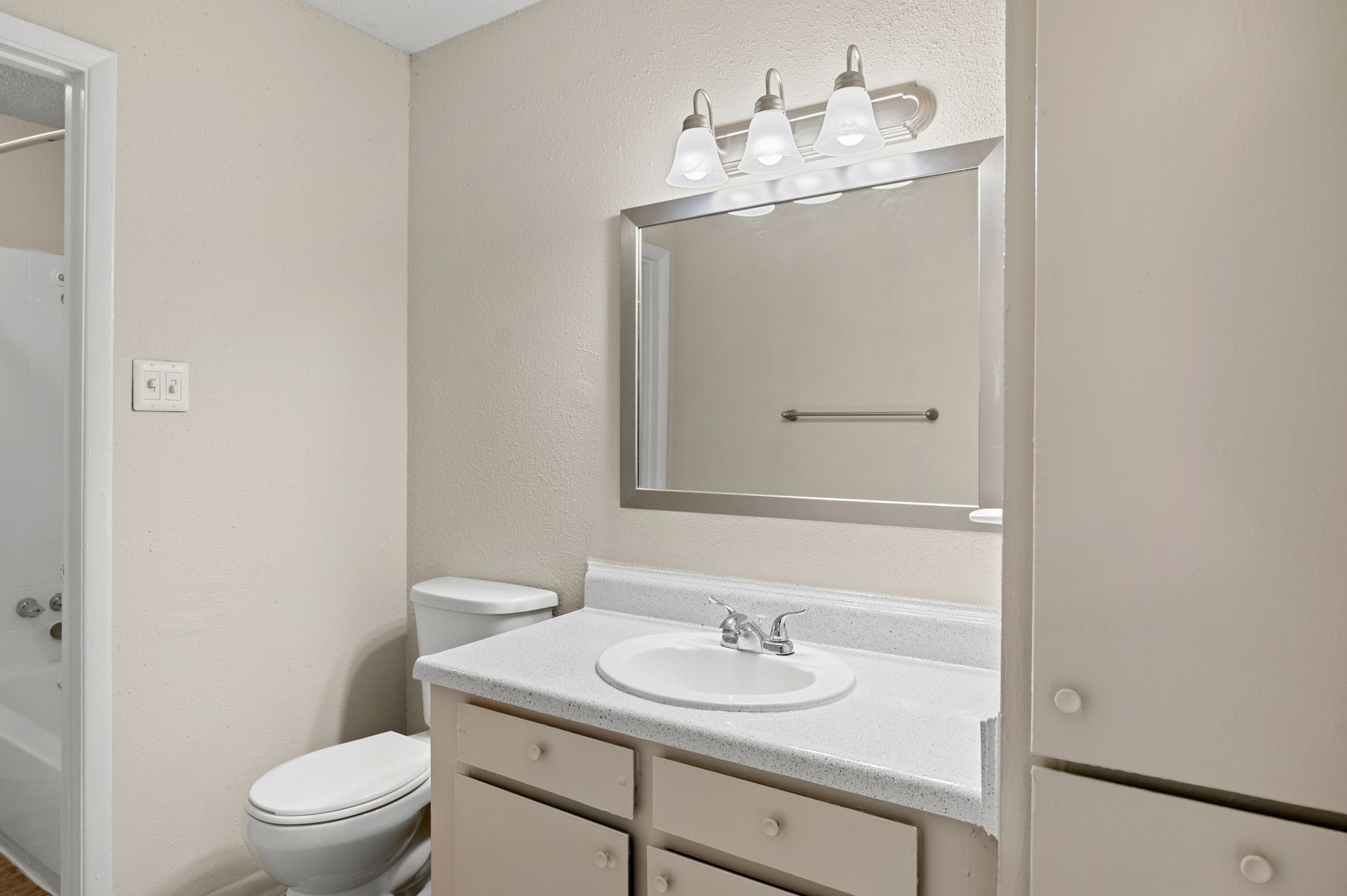 Bathroom with a toilet, sink, mirror, and cabinet. Neutral colors, overhead lighting, and white fixtures.