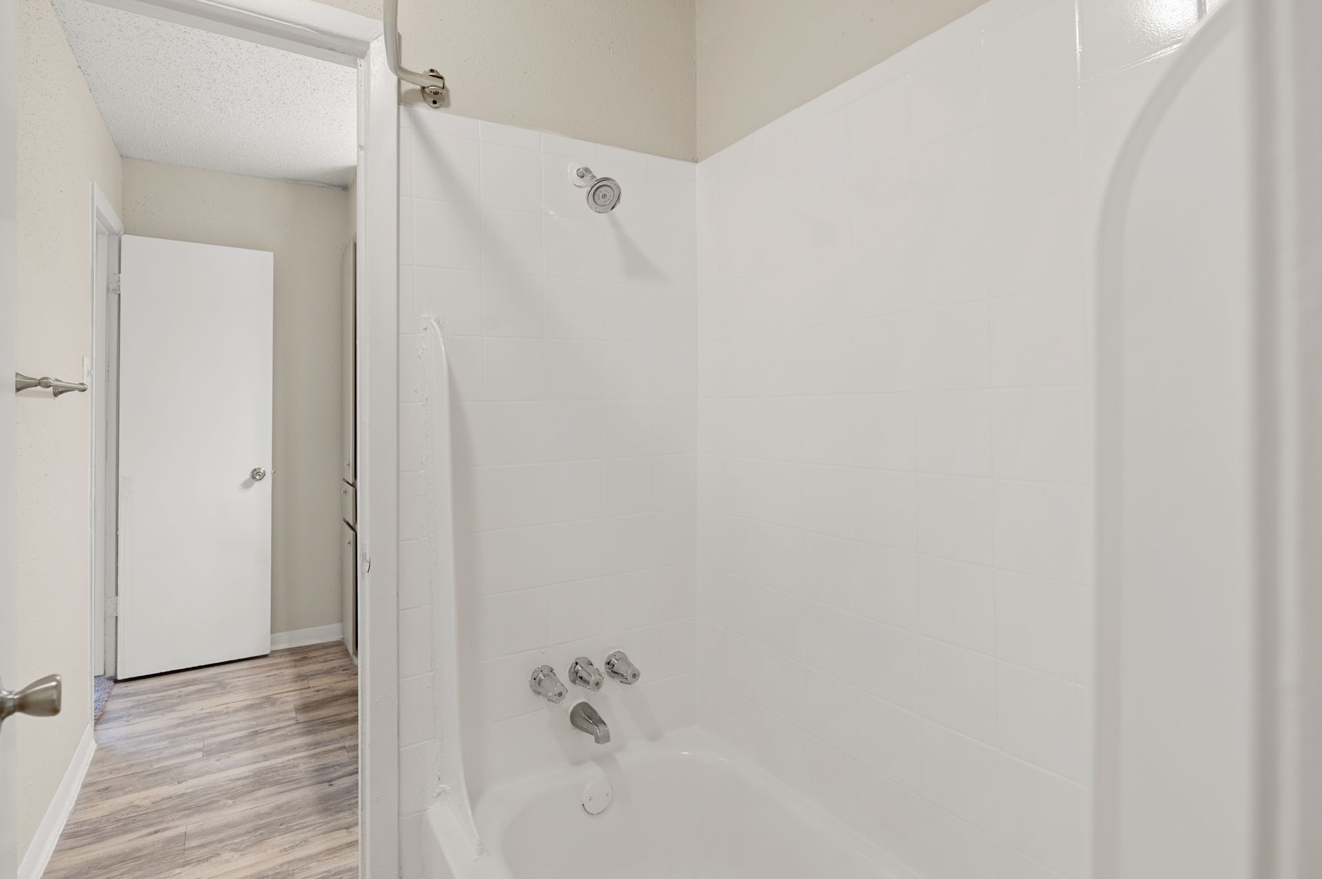 White bathtub and shower with fixtures, partially obscured by a shower curtain, next to a hallway with a closed door.