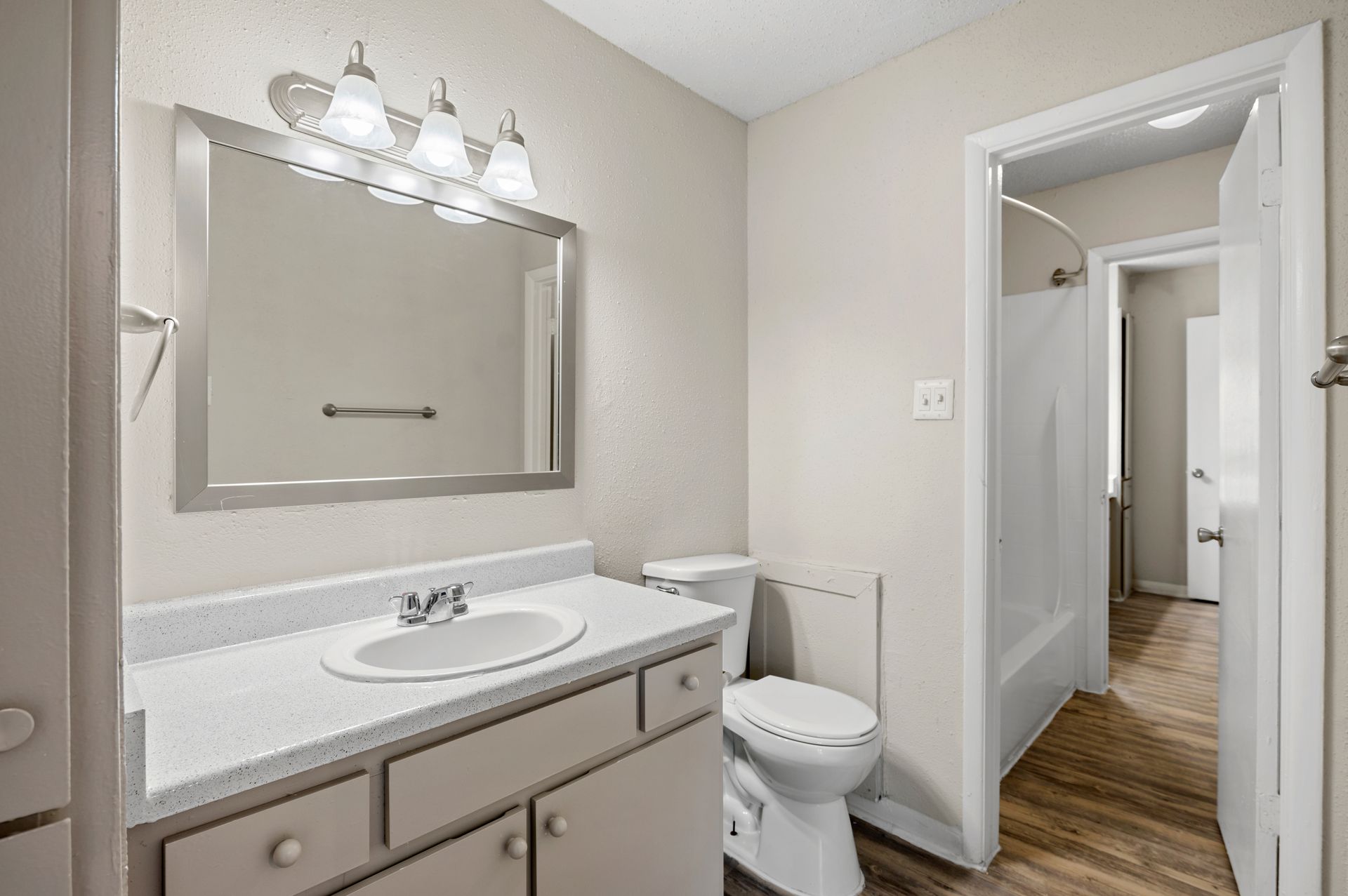 Bathroom with a sink, toilet, and bathtub. Light fixtures above a mirror and neutral color walls.