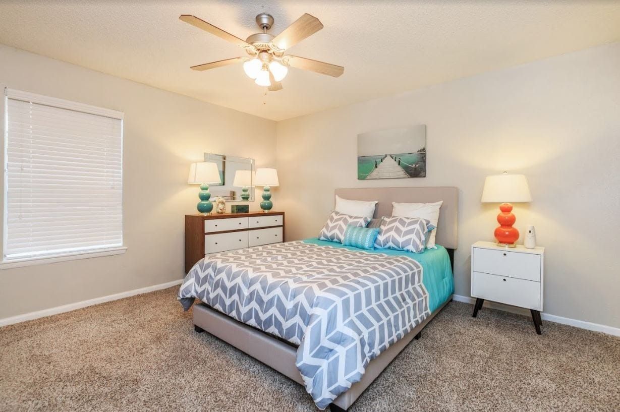 Bedroom with bed, dresser, nightstand, lamps, and a ceiling fan.