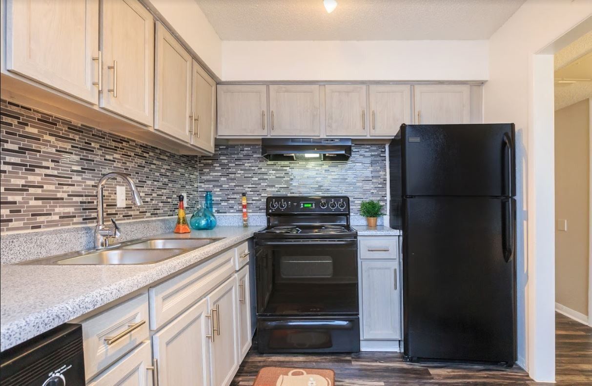 Kitchen with gray cabinets, black appliances, speckled countertops, and tile backsplash.