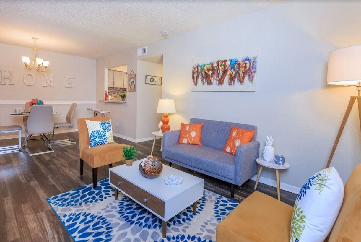 Living room with blue sofa, orange chairs, coffee table, and colorful rug.