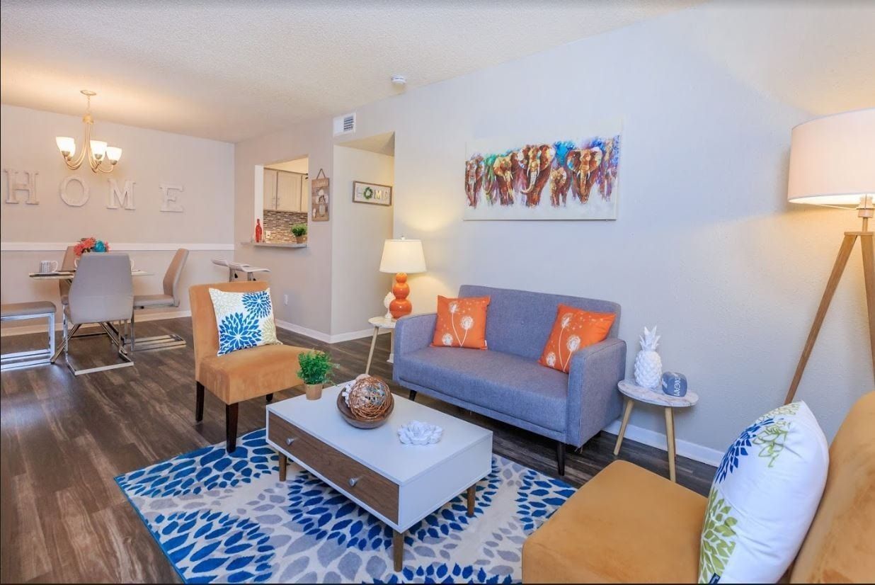 Living room with blue and orange accents: sofa, chairs, rug, and art. Dining area visible.