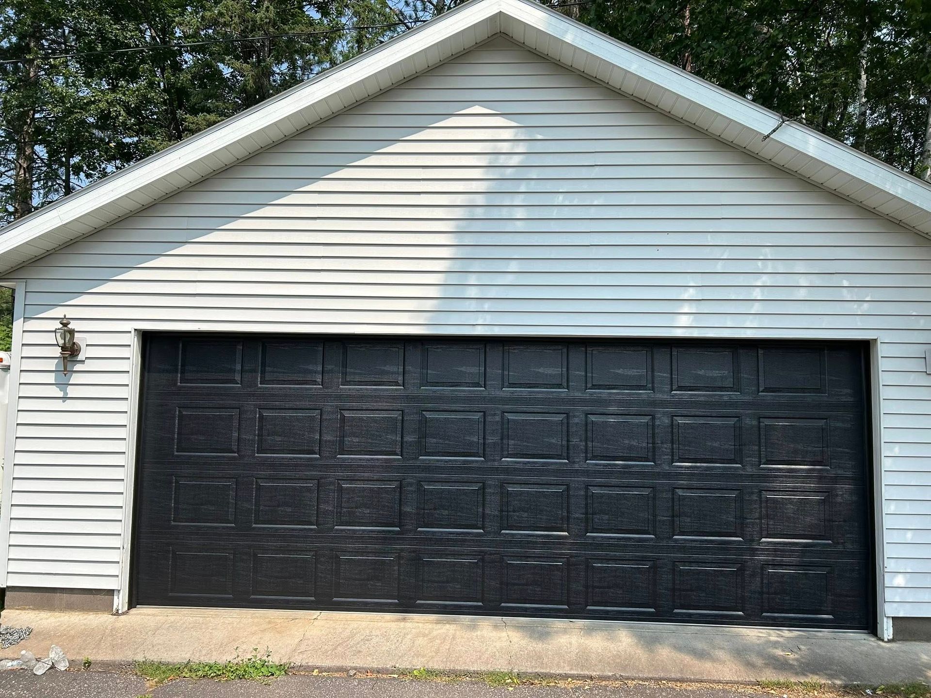 Black garage door on a white-sided building with a gabled roof, set outdoors on a sunny day.