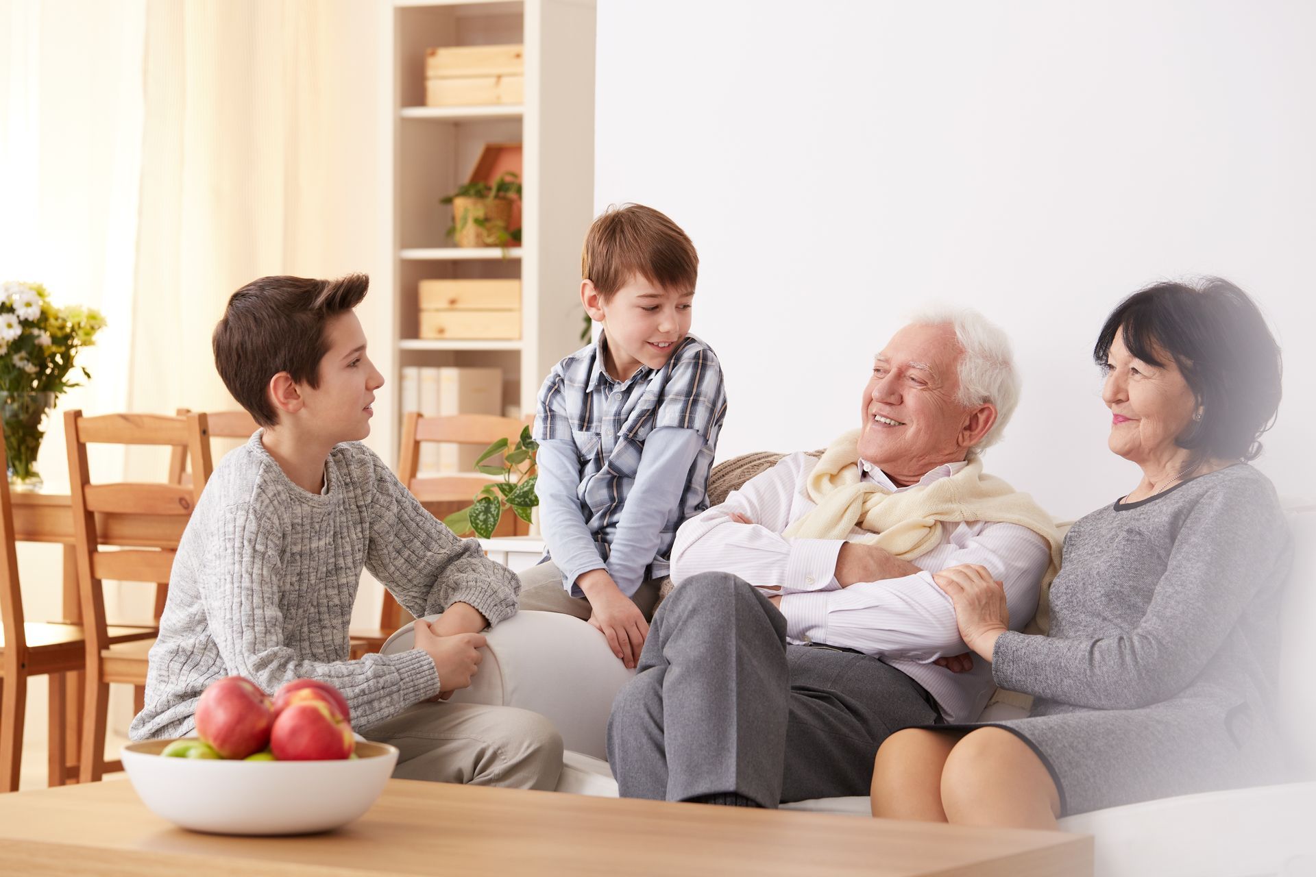 Family sitting and talking in a living room; a boy and two grandparents on a couch and another boy stands.