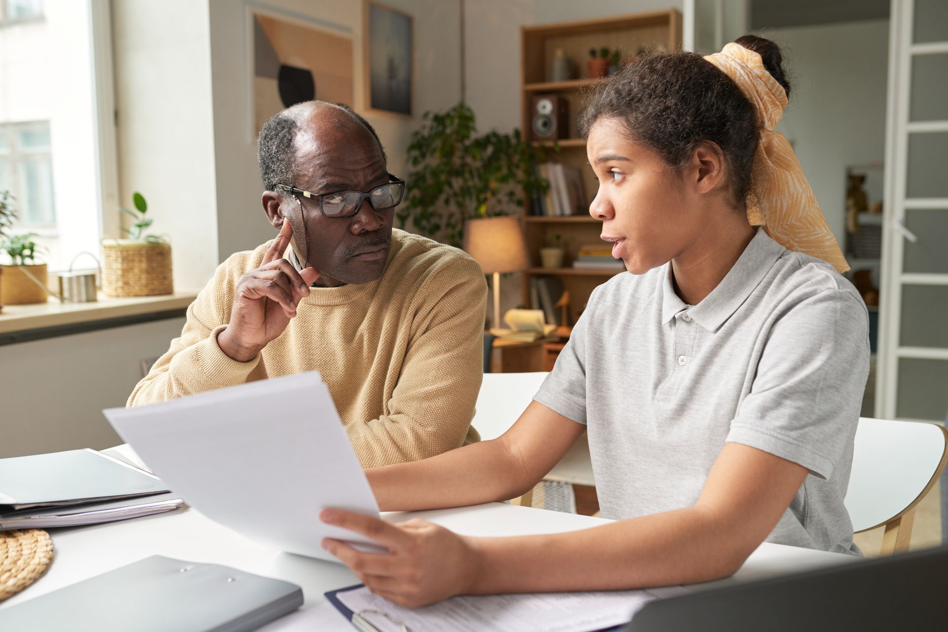 A young person explaining documents to an older person at a table, indoor setting.
