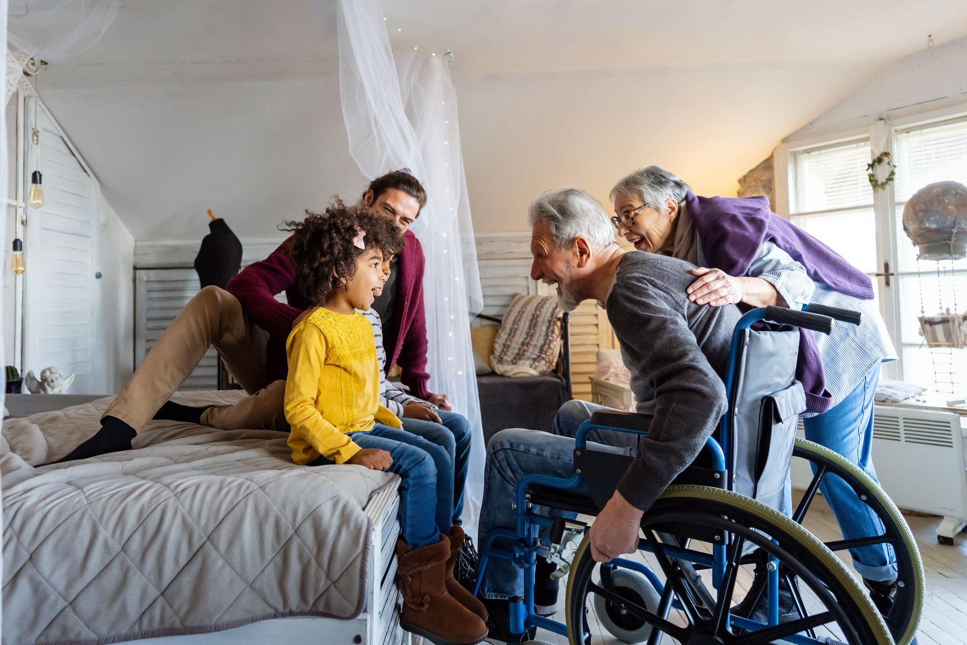Family visits an older person in a wheelchair indoors; child, adult, and another older person stand nearby.