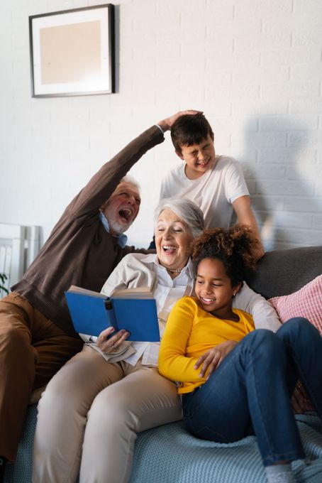 Grandparents and grandchildren on a couch, reading a book and laughing.