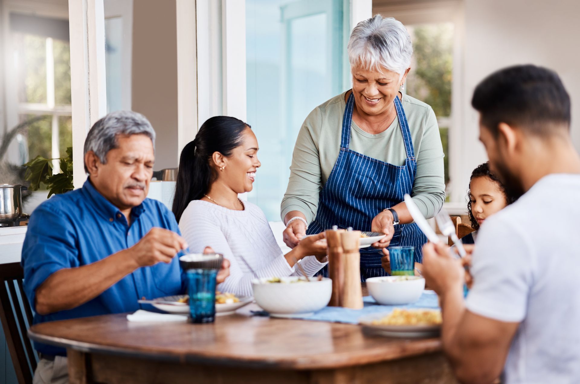 Family gathering around a wooden table; woman serving food.