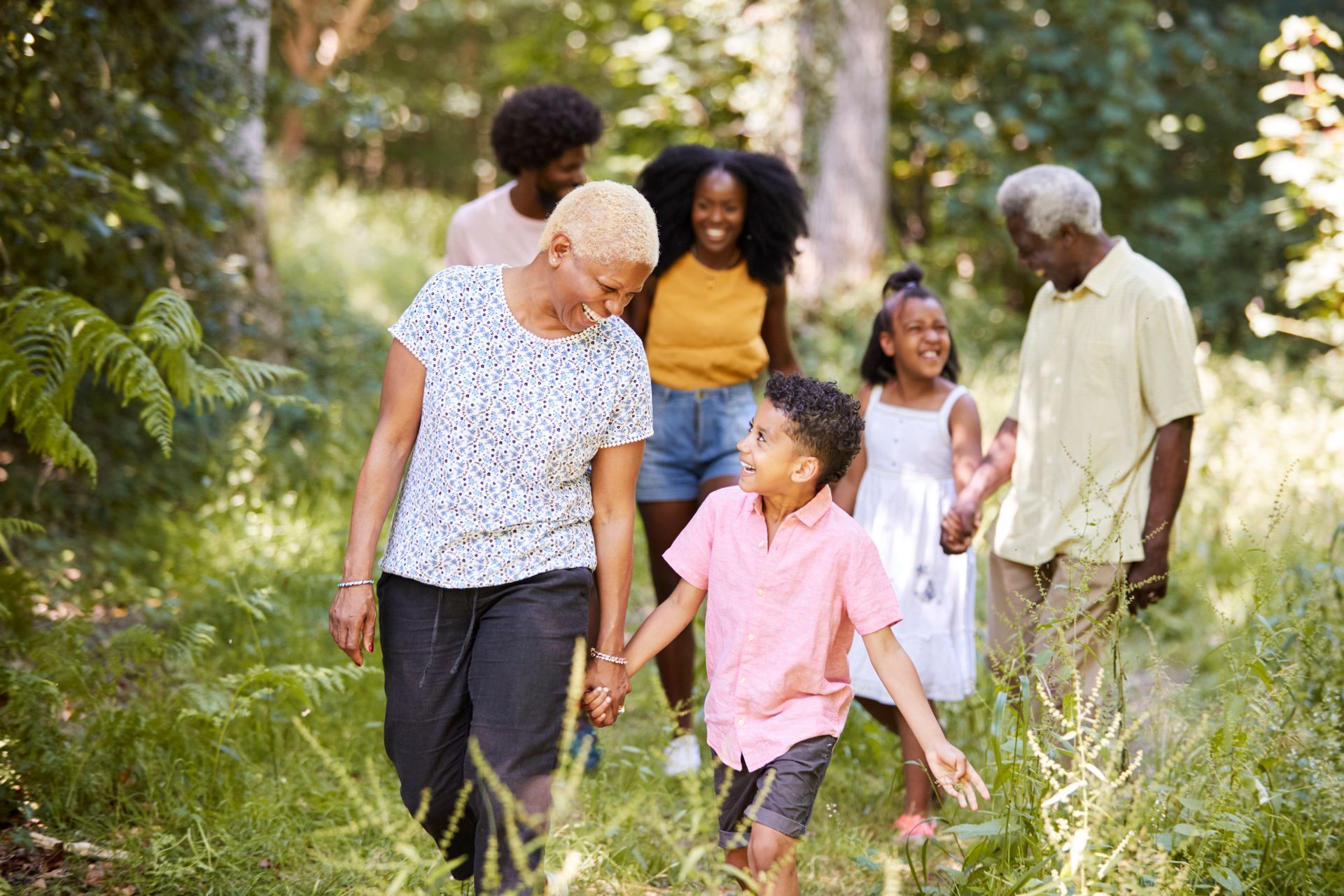 Family of six walking together on a trail in a forest; sunny day.
